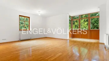 Helles Wohnzimmer mit Parkettboden, weißen Wänden und großen Fenstern mit Blick ins Grüne.