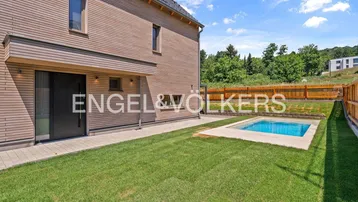 Modernes Haus mit Holzfassade, kleinem Pool und gepflegtem Rasen im Gartenbereich.
