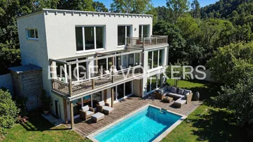 Moderne Villa mit mehreren Terrassen, großem Pool und umgebender Grünfläche.