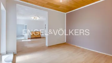 Geräumiges Wohnzimmer mit hellem Laminatboden und Holzdeckenverkleidung, offen zu weiteren Räumen.