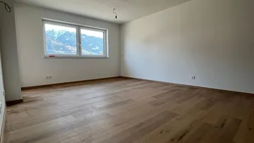 Helles, leeres Zimmer mit Holzboden und weiten Fenstern mit Bergblick.