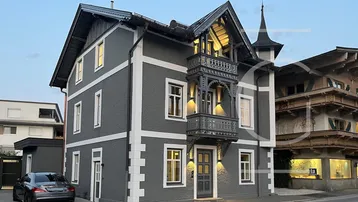Modernisiertes Gebäude mit dunkler Fassade, weißen Akzenten und einem verzierten Balkon bei Abendlicht.