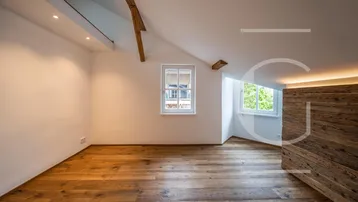 Gemütlicher Raum im Dachgeschoss mit Holzdielenboden, Dachschrägen und einem Fenster mit Grünblick.