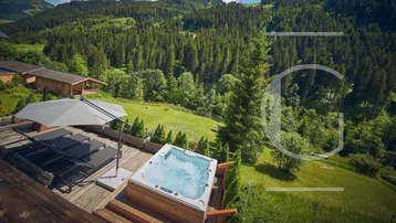 Panoramablick auf die Holzterrasse mit Whirlpool und Liegestühlen inmitten der Berglandschaft.