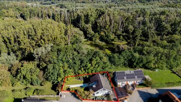 Luftaufnahme eines Hauses mit Solaranlage, umgeben von viel Grün und Wald in ländlicher Umgebung.