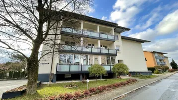 Mehrfamilienhaus mit mehreren Balkonen und gepflegter Außenanlage unter bewölktem Himmel.