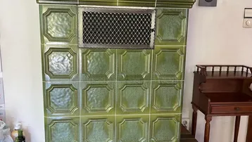 Traditioneller grüner Kachelofen auf gemauertem Sockel als Wärmequelle im Wohnbereich.