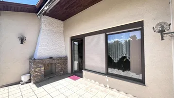 Sonniger Terrassenbereich mit Fliesenboden, Außenkamin und Zugang zum Innenbereich.