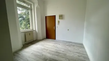 Helles Zimmer mit Laminatboden und großem Fenster, das viel Tageslicht hereinlässt.