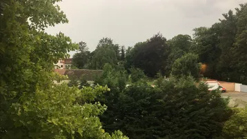 Weitläufiger Blick ins Grüne mit vielen Bäumen und einem bewölkten Himmel.