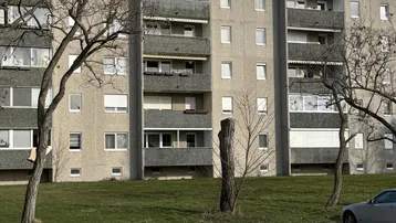 Mehrfamilienhaus mit Balkonen und Grünflächen, umgeben von Bäumen und einem Parkplatz.