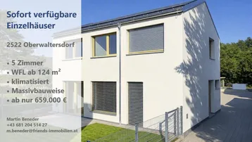 Modernes Einfamilienhaus mit heller Fassade, Rollläden, Photovoltaikanlage und gepflegtem Vorgarten, umgeben von viel Grün.