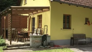 Gelbes Landhaus mit überdachter Terrasse und Gartenbereich, umgeben von viel Grün.