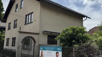 Gut erhaltenes Einfamilienhaus mit Satteldach und grüner Umgebung, umgeben von einem Zaun.