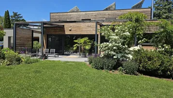 Modernes Haus mit Holzfassade, großem Garten und sonniger Terrasse mit Sitzgelegenheiten.