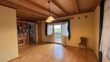 Geräumiges Wohnzimmer mit Holzbalkendecke, Parkettboden und Zugang zu einem Balkon mit Weitblick.