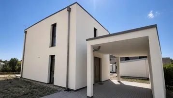 Modernes Einfamilienhaus mit Flachdach und integriertem Carport unter strahlendem Sonnenschein.