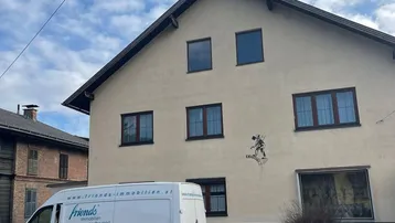Wohnhausfassade mit Satteldach und braunen Fenstern, von der Straße aus gesehen.