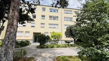 Mehrfamilienhaus mit gepflegter Fassade und Grünflächen im Eingangsbereich.