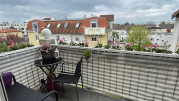 Möblierter Balkon mit Granitfliesen und Blick auf die umliegenden Dächer und Gebäude.