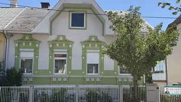 Vorderansicht eines charmanten Hauses mit grüner Fassade und dekorativen Elementen unter blauem Himmel.