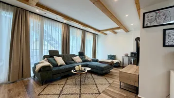 Gemütliches Wohnzimmer mit großem Sofa, Holzbalken und Zugang zu einem Außenbereich.