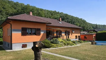 Haus mit orangefarbener Fassade, braunem Dach und einem gepflegten Gartenbereich im Grünen.