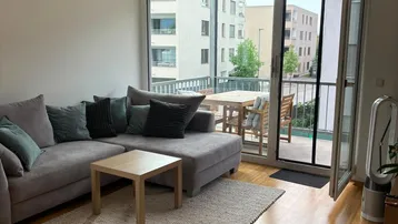 Helles Wohnzimmer mit gemütlichem Sofa, Holzboden und direktem Zugang zum Balkon mit Außenbereich.