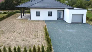Neubau-Einfamilienhaus mit dunklem Dach, integrierter Garage und unfertigem Gartenbereich.