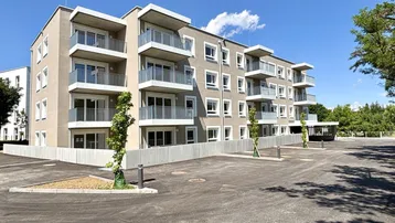 Modernes Mehrfamilienhaus mit mehreren Balkonen und Außenparkplätzen unter blauem Himmel.