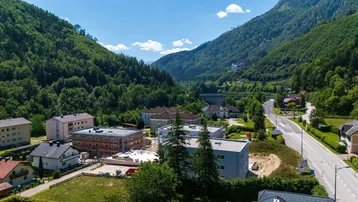 Weitläufige Luftaufnahme einer Baustelle in einem Tal, umgeben von Bergen, Häusern und einer Straße.