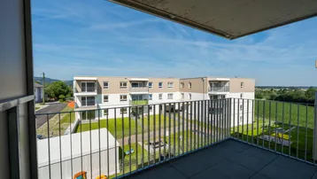 Blick vom Balkon auf die moderne Wohnanlage mit grüner Umgebung und Feldern.