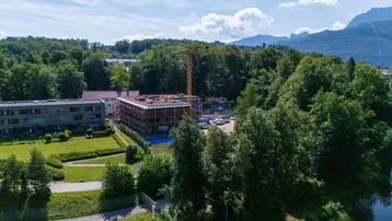Weitläufige Luftaufnahme der Baustelle mit See, Bergen und üppiger grüner Umgebung.