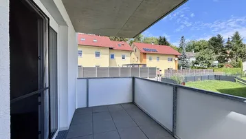 Geräumiger Balkon mit Fliesenboden und Blick auf die umliegende Wohngegend und viel Grün.