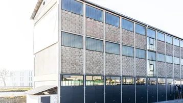 Industrielles Gebäude mit Betonfassade, großen Glasfenstern und mehreren dunklen Lagertoren im Erdgeschoss.