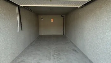 Leere Einzelgarage mit Betonboden und weißem Sektionaltor, bereit zur Nutzung.