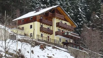 Traditionelles Alpenhaus mit Holzbalkonen und Satteldach, umgeben von verschneiten Wäldern.