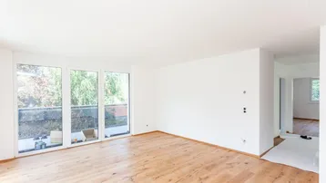Heller Wohnraum mit Eichenparkett und großen Fenstern mit Zugang zum Balkon.