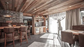 Gemütlicher Wohn- und Essbereich im Chalet-Stil mit Holzbalkendecke und Steinwand.