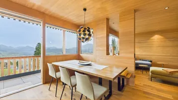 Heller Essbereich mit Holzwänden und -decke, großem Esstisch und Bergblick von der Terrasse.