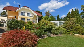 Großzügiges Anwesen mit gepflegtem Garten, Poolüberdachung und sonniger Fassade unter blauem Himmel.