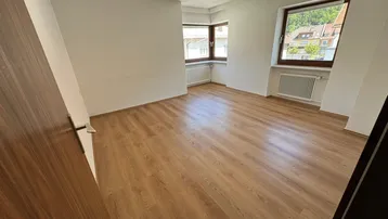 Helles Zimmer mit Laminatboden und zwei Fenstern, die einen Blick auf die Umgebung bieten.