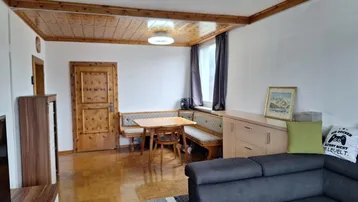 Gemütlicher Wohn-Essbereich mit Holzbalkendecke, Parkettboden und traditioneller Sitzecke am Fenster.