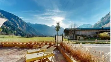 Sonnige Terrasse mit Liegestühlen und weitem Blick auf die umliegenden Berge und grüne Felder.