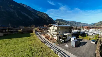 Gebäudeansicht in ländlicher Umgebung mit Parkplätzen und Bergblick.