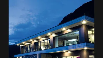 Moderne Gewerbeimmobilie bei Nacht mit beleuchteten Fenstern und einer klaren, zeitgenössischen Architektur in bergiger Umgebung.