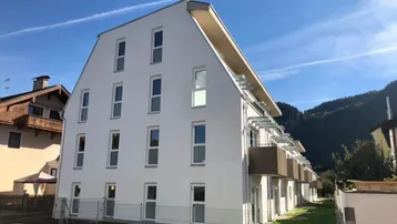 Modernes Mehrfamilienhaus mit weißer Fassade und Balkonen in bergiger Umgebung.
