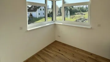 Heller Raum mit Holzboden und großen Eckfenstern, bietet viel natürliches Licht.