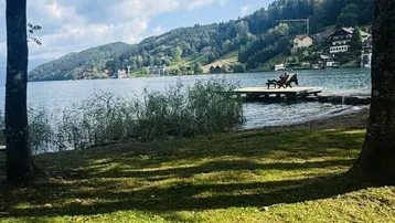 Idyllischer Seeblick mit Bergen im Hintergrund und einem kleinen Steg am Ufer.