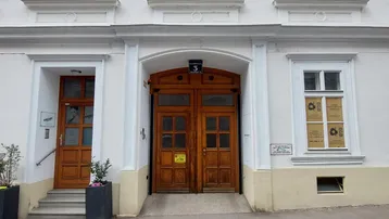 Historische Fassade eines Gebäudes mit eleganten Fenstern und zwei Holztüren im Eingangsbereich.